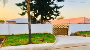 A residential area with a gated entrance, a paved driveway, and a grassy lawn. - UNCLE CHARLES GUESTHOUSE (Pretoria)