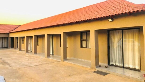 A building with a red-tiled roof, multiple rooms with sliding glass doors, and a concrete ground floor. - UNCLE CHARLES GUESTHOUSE (Pretoria)
