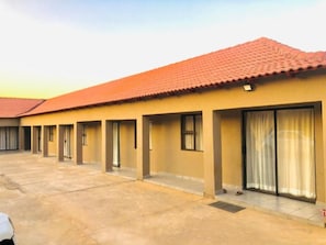 A building with a red-tiled roof, multiple rooms with sliding glass doors, and a concrete ground floor. - UNCLE CHARLES GUESTHOUSE (Pretoria)