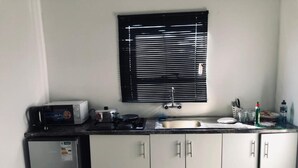 A compact kitchen with a refrigerator, microwave, sink, and cabinets. - UNCLE CHARLES GUESTHOUSE (Pretoria)