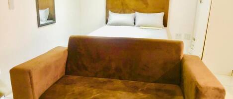 A room with a bed, a brown sofa, and a mirror on the wall.