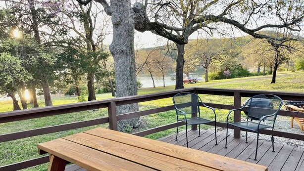 A wooden deck with a picnic table and chairs, overlooking a grassy area and a body of water. - Cozy Cottage - Lakeview (Reeds Spring)