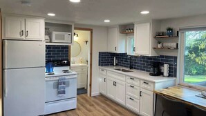 A modern kitchen with white cabinets, a microwave, a stove, and a sink. - Cozy Cottage - Lakeview (Reeds Spring)