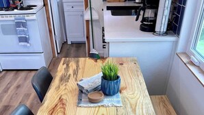 A wooden dining table with a plant centerpiece, black chairs, and a kitchen in the background. - Cozy Cottage - Lakeview (Reeds Spring)