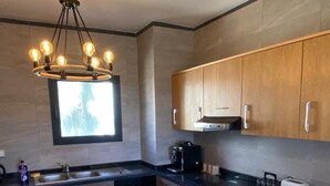A modern kitchen with wooden cabinets, a black countertop, a built-in oven, a coffee maker, and a bowl on the counter. - Magnificent Duplex Sea View in Taghazout Bay (Taghazout)