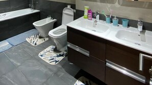 A modern bathroom with a bathtub, toilet, bidet, and vanity with a large mirror. - Magnificent Duplex Sea View in Taghazout Bay (Taghazout)