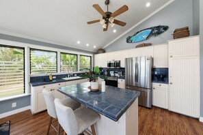 A kitchen with a central island, white cabinetry, stainless steel appliances, and a ceiling fan. - SUMMER SALE! Spacious 2BD Cottage Walk to Kaanapali Beach - ICC 2 (Lahaina)