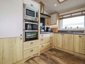 A kitchen with wooden cabinets, stainless steel appliances, a window, and a sink. - 8 Summerleaze (Bude)