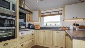 A kitchen with wooden cabinets, a built-in oven, a sink, and a window with a view. - 8 Summerleaze (Bude)