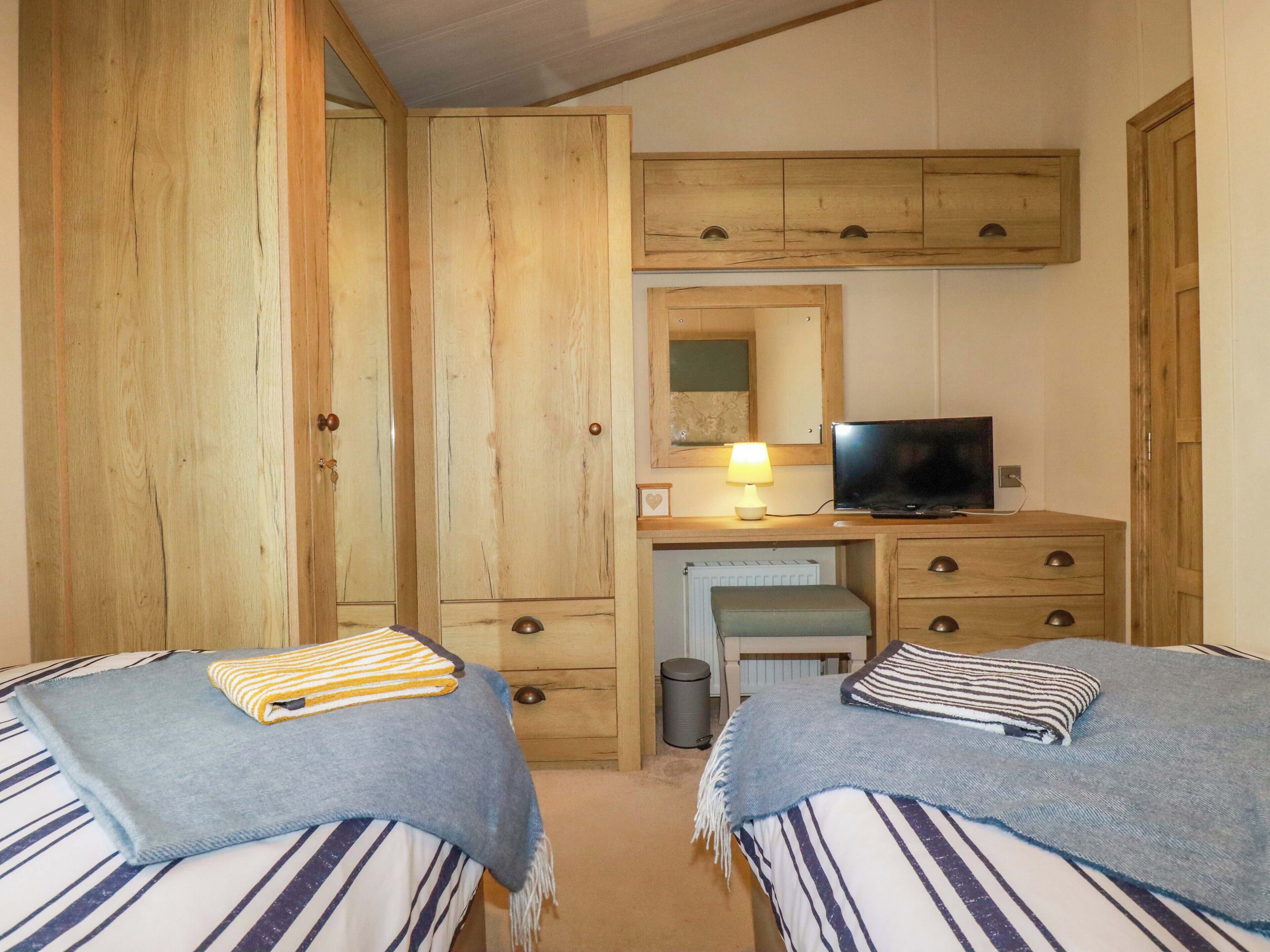 Ein Schlafzimmer mit zwei Betten, einem Fernseher, einem Holzschrank und einem Schreibtisch mit Lampe.