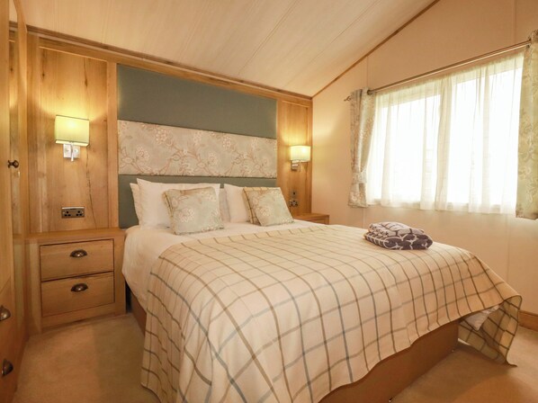 A bedroom with a bed, bedside lamps, a nightstand, a drawer, and a window with curtains. - 8 Summerleaze (Bude)