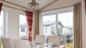 A dining area with a table set for four, chairs, a ceiling fan, and large windows with curtains. - 8 Summerleaze (Bude)
