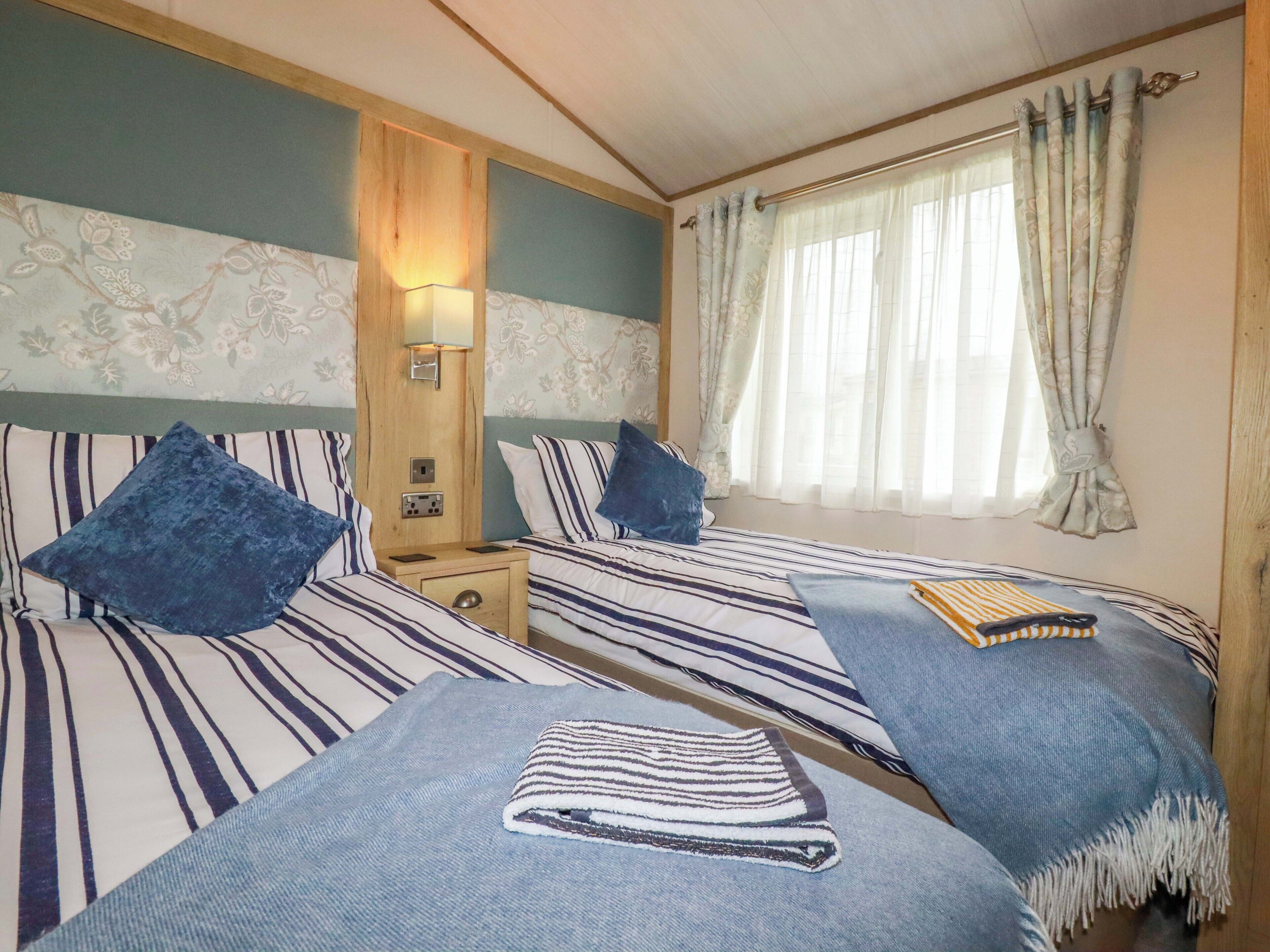 A double room with two beds, a nightstand, a lamp, and a window with curtains.
