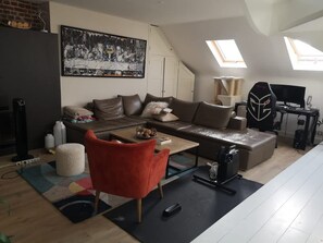 A modern living room with a sectional sofa, a red armchair, a painting, and a gaming setup. - Bail Mobilit Grand Loft Hypercentre de Lille (Lille)