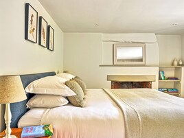 A neatly arranged bedroom with a bed, pillows, a bedside lamp, a fireplace, framed pictures, and a bookshelf.
