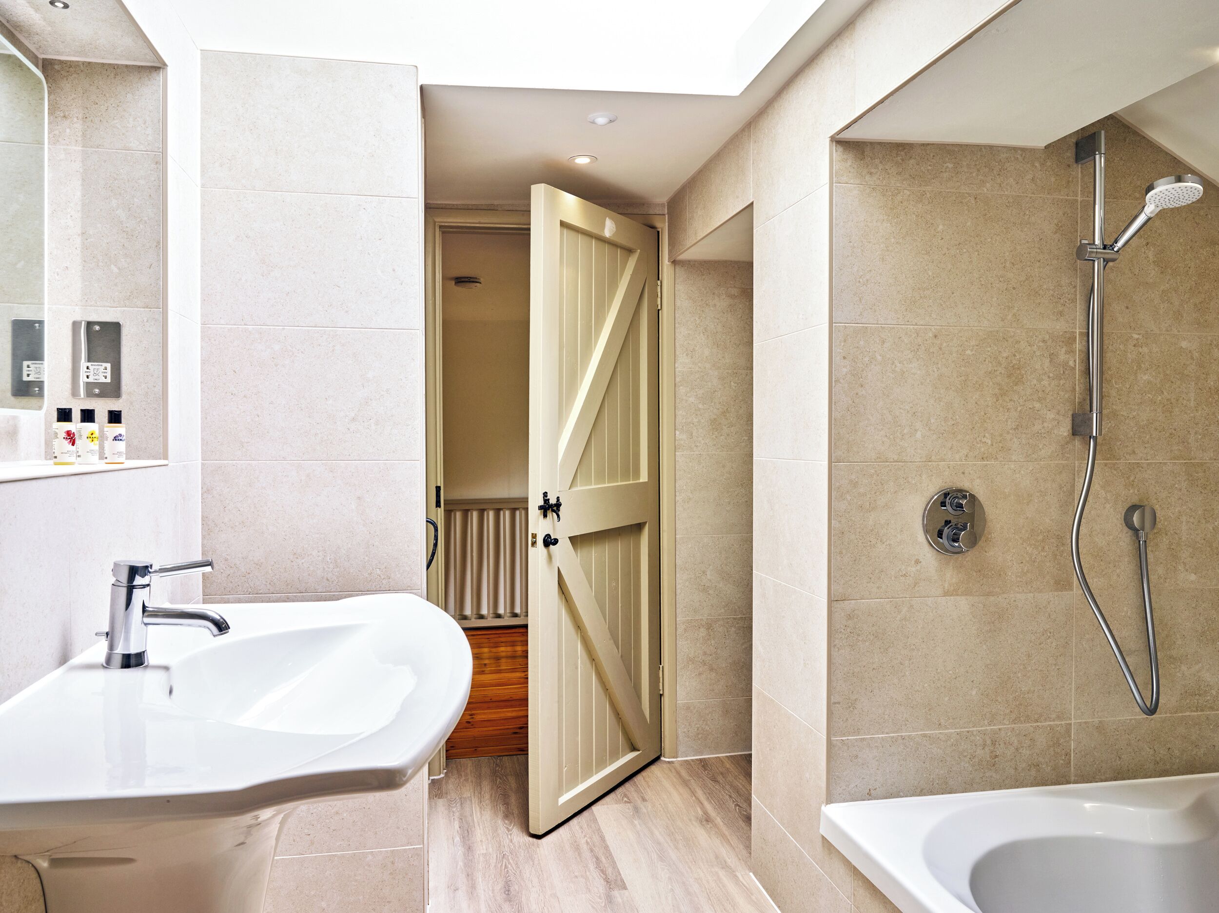 Un baño moderno con ducha, lavamanos y una puerta que da a otra habitación.