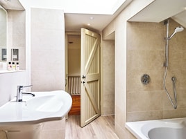 Un baño moderno con ducha, lavamanos y una puerta que da a otra habitación.