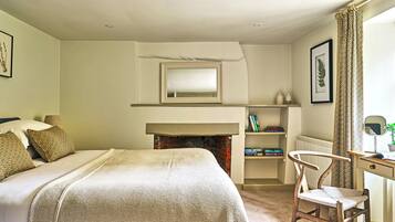 A bedroom with a bed, a chair, a desk, a fireplace, and a mirror.