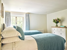 Un dormitorio con dos camas, un aparador, una ventana con cortinas y un florero con flores.