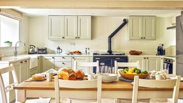 A kitchen with white cabinets, a wooden dining table, and chairs. There is a stove, a sink, and various kitchen items on the countertops.