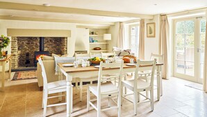 Un comedor con chimenea de piedra, mobiliario blanco y vistas amplias por grandes ventanales.