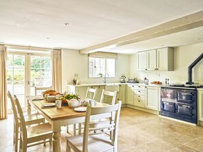 A kitchen with a dining table, chairs, a stove, and a window with curtains. - Gitcombe Coach House (Totnes)