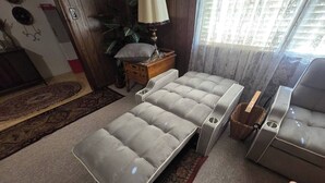 A room with a sofa, a small table, a lamp, and a window with curtains. - This cozy 3 bed 2 bath house will remind you of a weekend at Grandmother's. (Albertville)