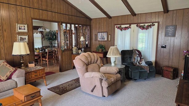 A cozy living room with a wooden paneled wall, a ceiling fan, a sofa, a chair, a small table with a lamp, and a rug. - This cozy 3 bed 2 bath house will remind you of a weekend at Grandmother's. (Albertville)