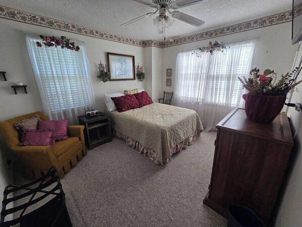 A bedroom with a bed, a nightstand, a dresser, a chair, and a window with curtains.