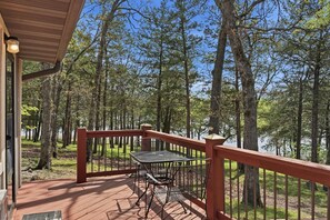 Une terrasse en bois avec une table et des chaises en métal, donnant sur une zone boisée avec un lac.
