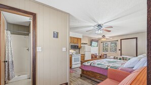 Una habitación compacta con cama, sofá, kitchenette y ventilador de techo.