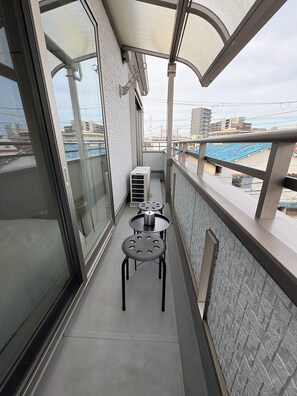 A balcony with a glass door, a metal railing, and a small table with chairs. - Perfect Base for Families - 3Bedrooms, 2Baths, Full-Kitchen, Free-P (大阪市)