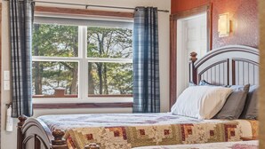 Un dormitorio con cama, cortinas, una ventana y una lámpara fijada a la pared.