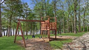 A playground with a swing set and climbing structure in a wooded park area. - Quail Cove 6 Lakefront Studio Boat Slip Optional (Shell Knob)