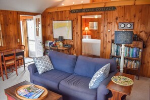 A cozy room with a blue sofa, a wooden bookshelf, a map on the wall, and a sign reading 'SWEET BEAGLE COTTAGE.' - Charming Cottage with Stunning Views and Steps to Red River Beach (Harwich)