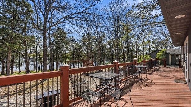 A wooden deck with outdoor seating, surrounded by trees and overlooking a body of water.
