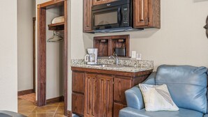 A compact kitchen with wooden cabinets, a microwave, a coffee maker, and a sink.