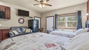 A bedroom with two beds, a ceiling fan, a television, a refrigerator, and a window with curtains.