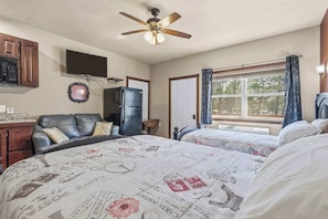 A bedroom with two beds, a ceiling fan, a television, a refrigerator, and a window with curtains.