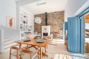 A modern living room with a stone wall, a fireplace, and a dining area with wooden furniture. - Ikos Kythnos (Kithnos)
