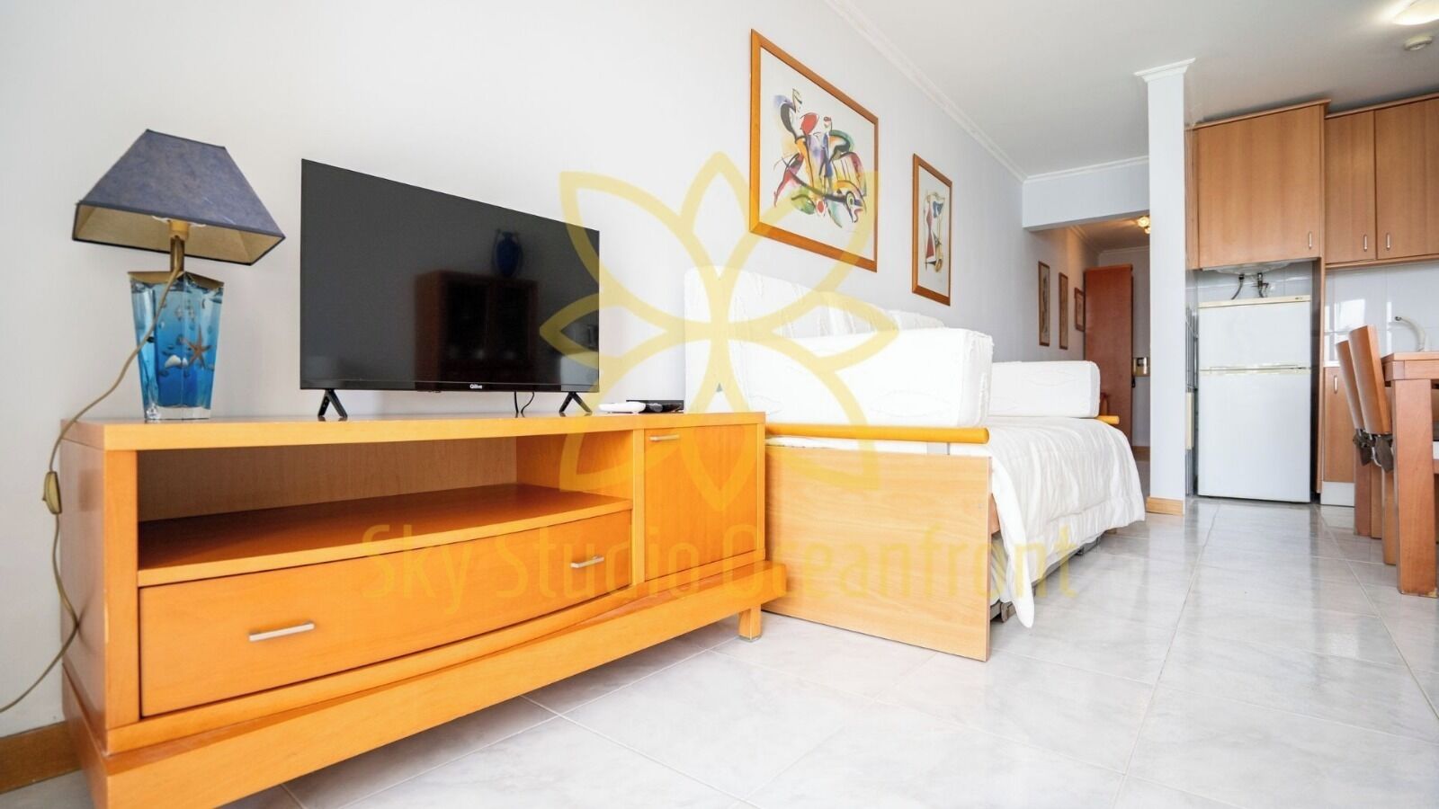 Een slaapkamer met een bed, een televisie, een houten dressoir en een keukenhoek.
