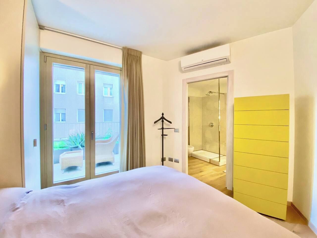 Ein Schlafzimmer mit Bett, einer Schiebetür zum Balkon, einem begehbaren Kleiderschrank und einem Duschbad.