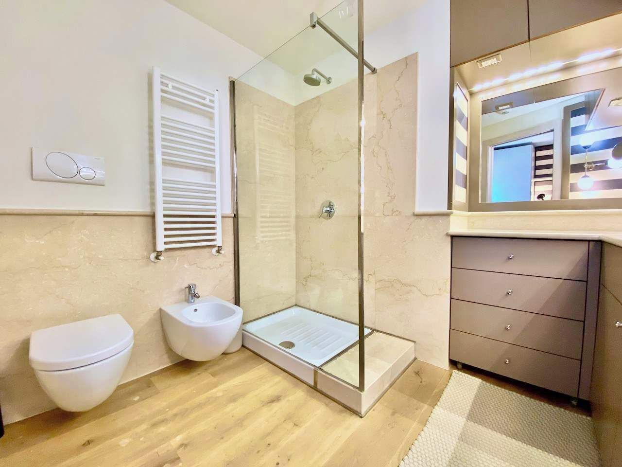 A modern bathroom with a glass-enclosed shower, a bidet, a toilet, and a vanity with drawers.
