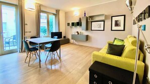 En moderne stue med spiseplads, en gul sofa og en sort fodskammel.
