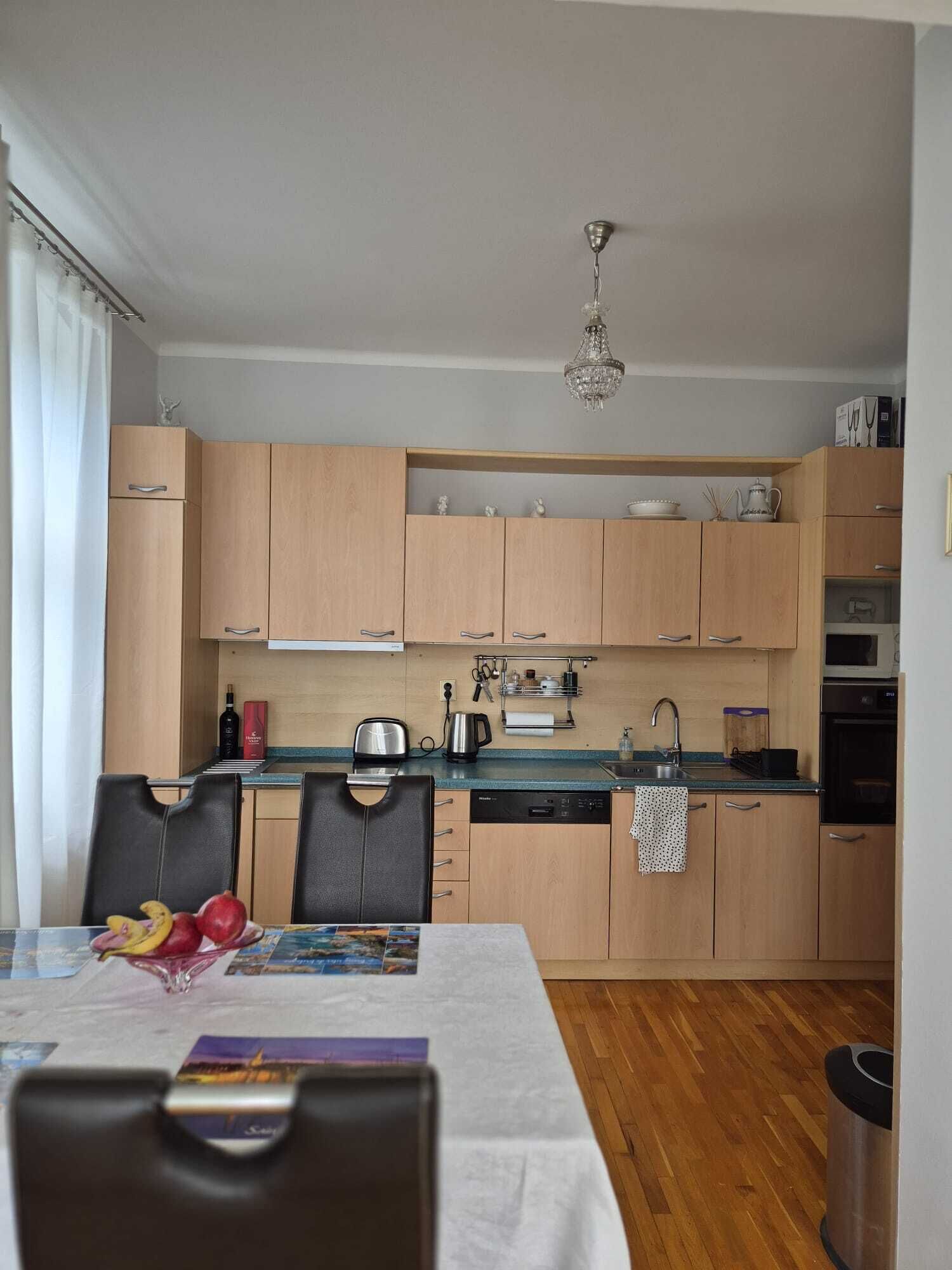 A compact kitchen with wooden cabinets, a dishwasher, a microwave, and a dining area with a table set for two.