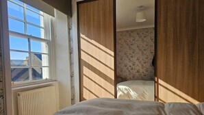 A bedroom with a bed, a radiator, a window, and a sliding door leading to another room.