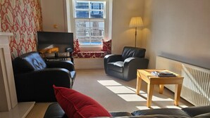 A living room with a sofa, two armchairs, a coffee table, a TV, and a window with a view.