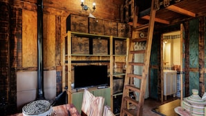 Un interior rústico con una pared de madera, un televisor sobre una estantería, una cesta tejida y una escalera.