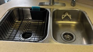Una cocina con un lavaplatos doble, un escurreplatos y una ventana con persianas.