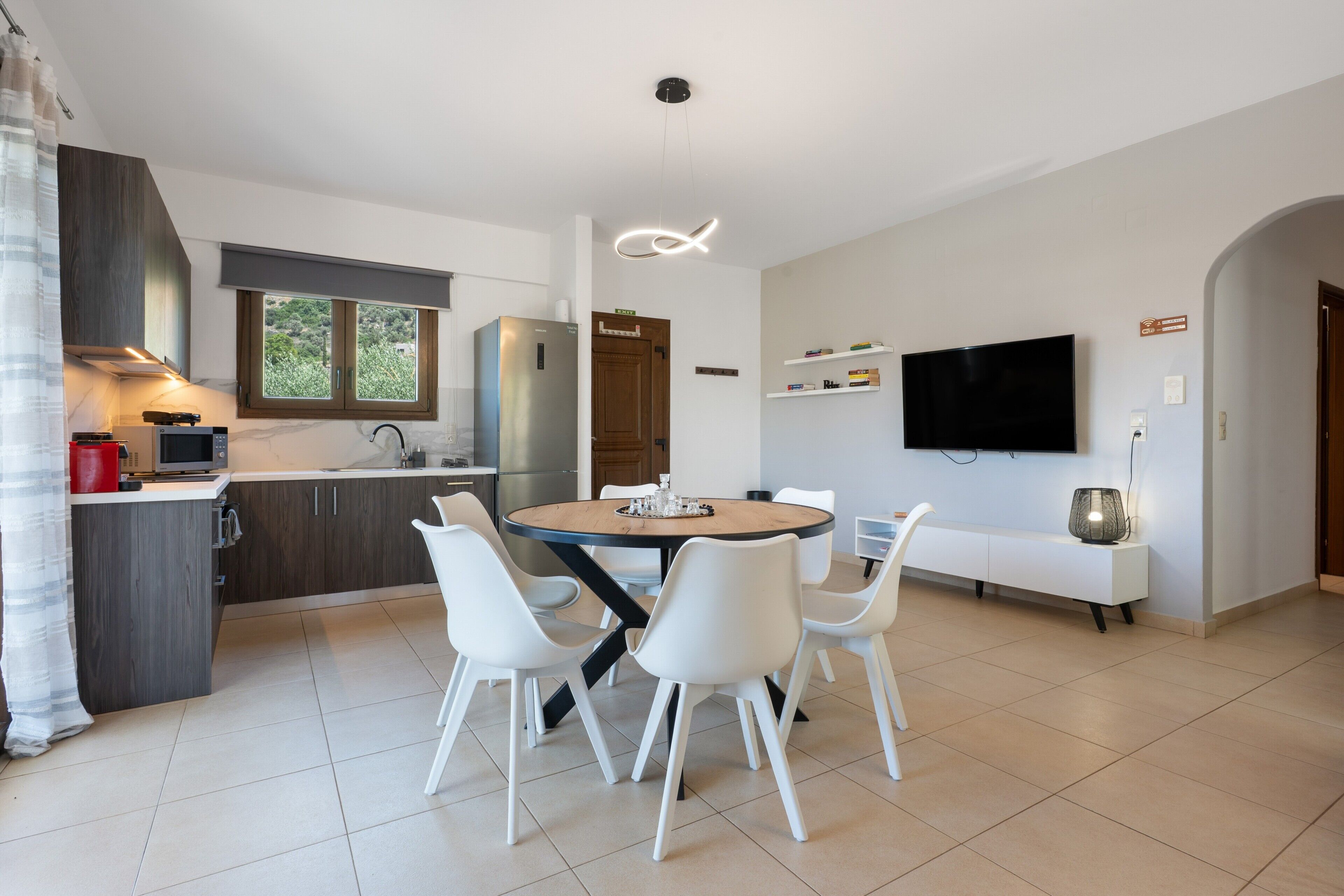 Une cuisine moderne avec des chaises blanches, une table à manger, un téléviseur à écran plat et un four encastré.